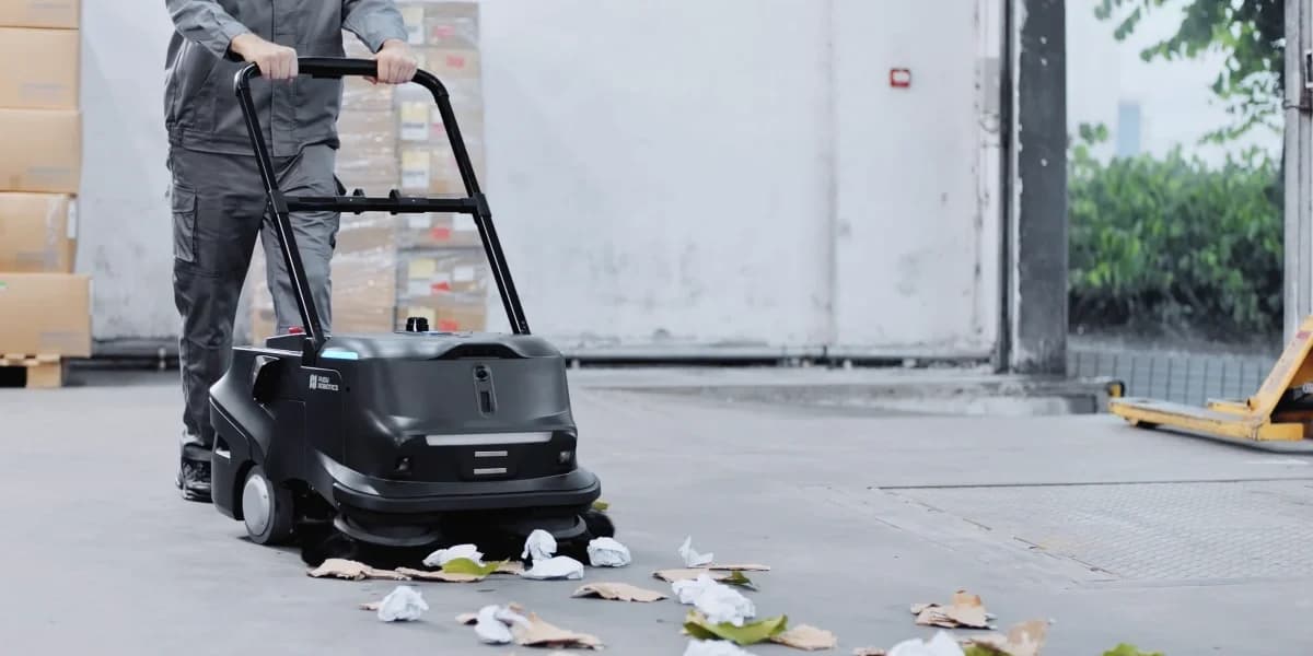 A person pushing a Pudu MT1 cleaning robot at a warehouse dock