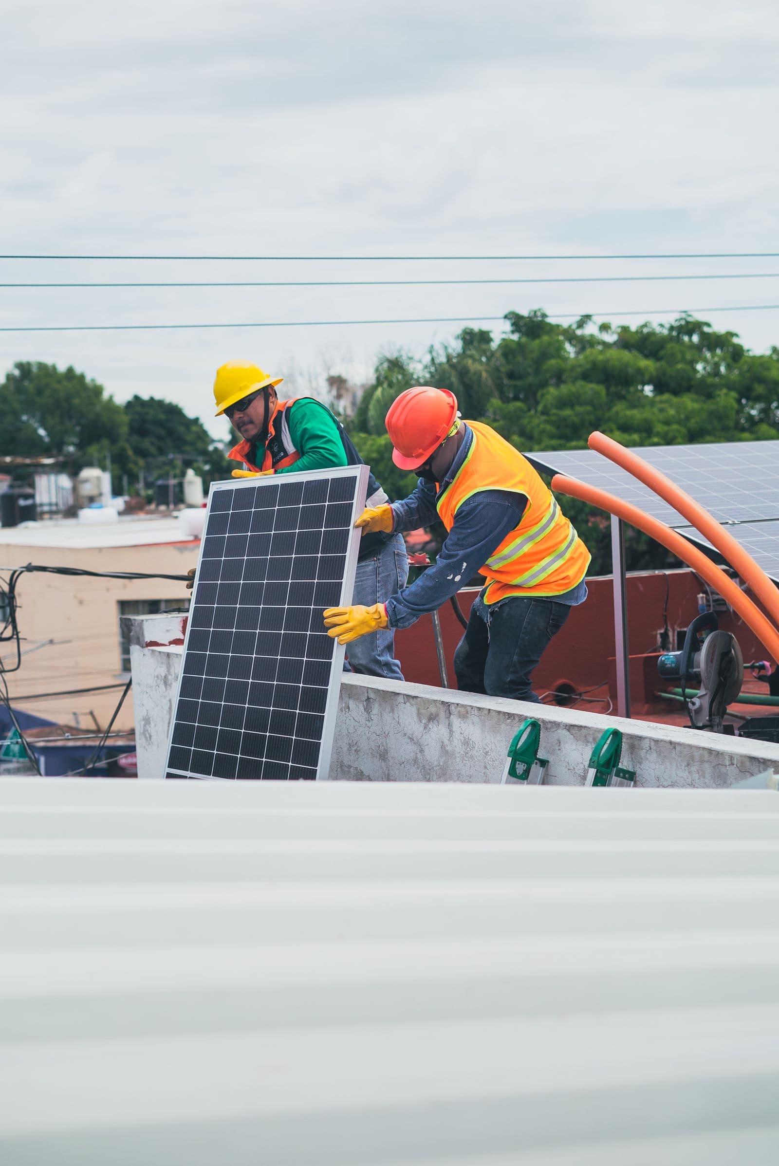 Two installers in hard hats and safety vests setting a solar panel into place on a rooftop.
