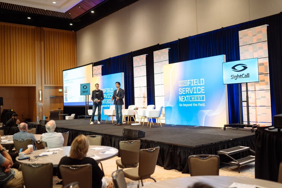 Wide view of a conference ballroom during a field-service industry event, with Aaryan speaking on stage.