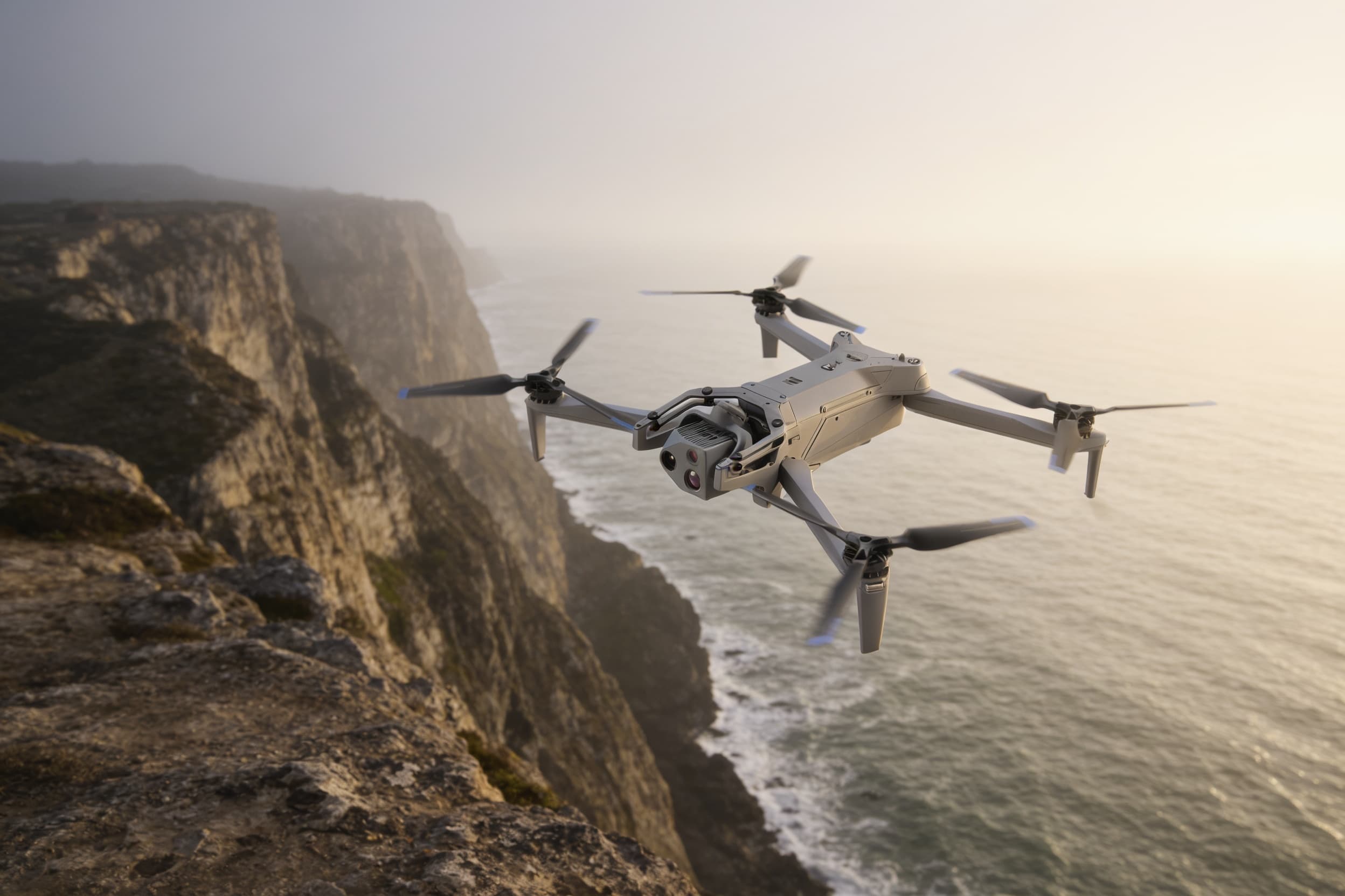 A fixed-wing inspection drone cruising a coastal cliff line in morning haze