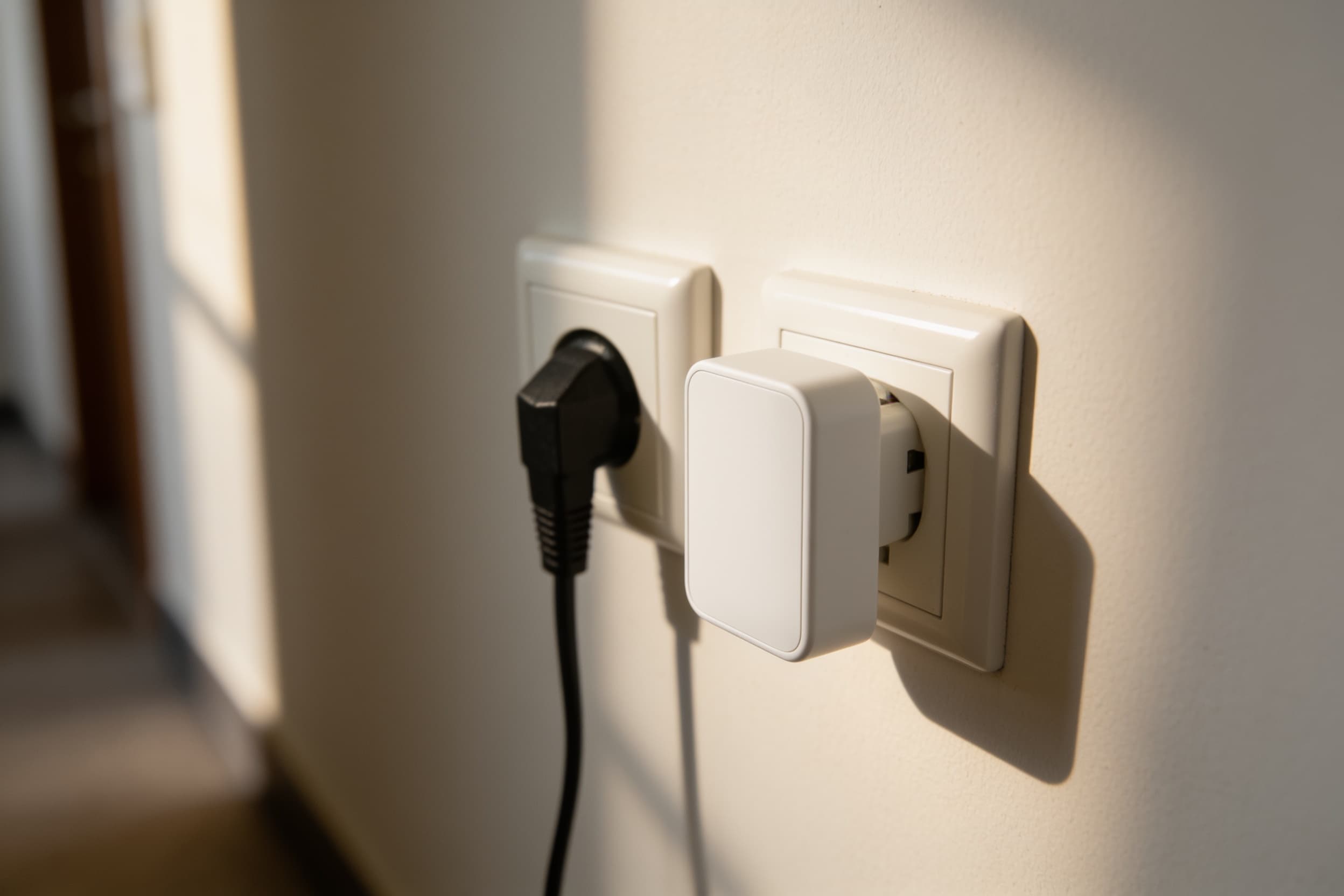 A wall-mounted security sensor plugged into a wall outlet mid-corridor