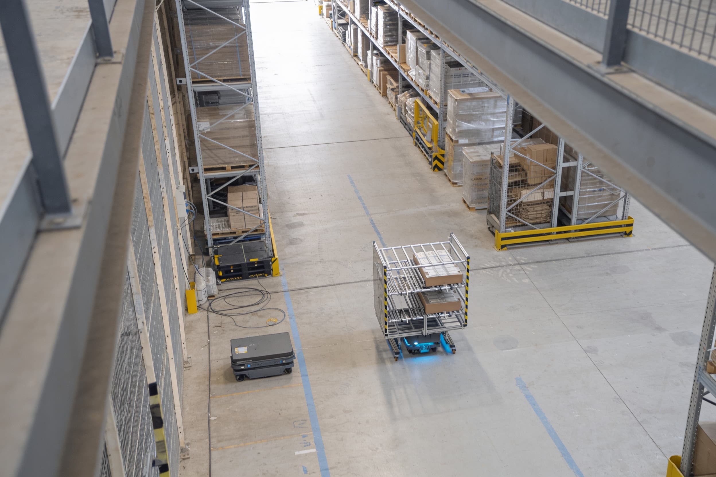 An autonomous mobile robot carrying a cart down a high-bay warehouse aisle