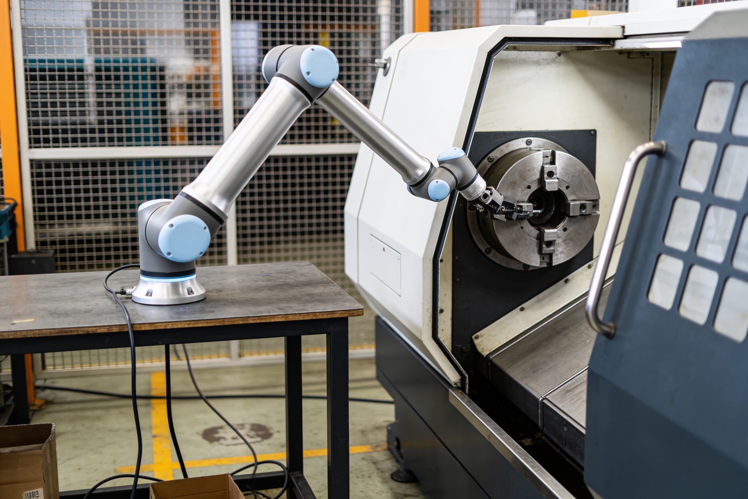 A collaborative robot arm tending a lathe on a machine-shop floor