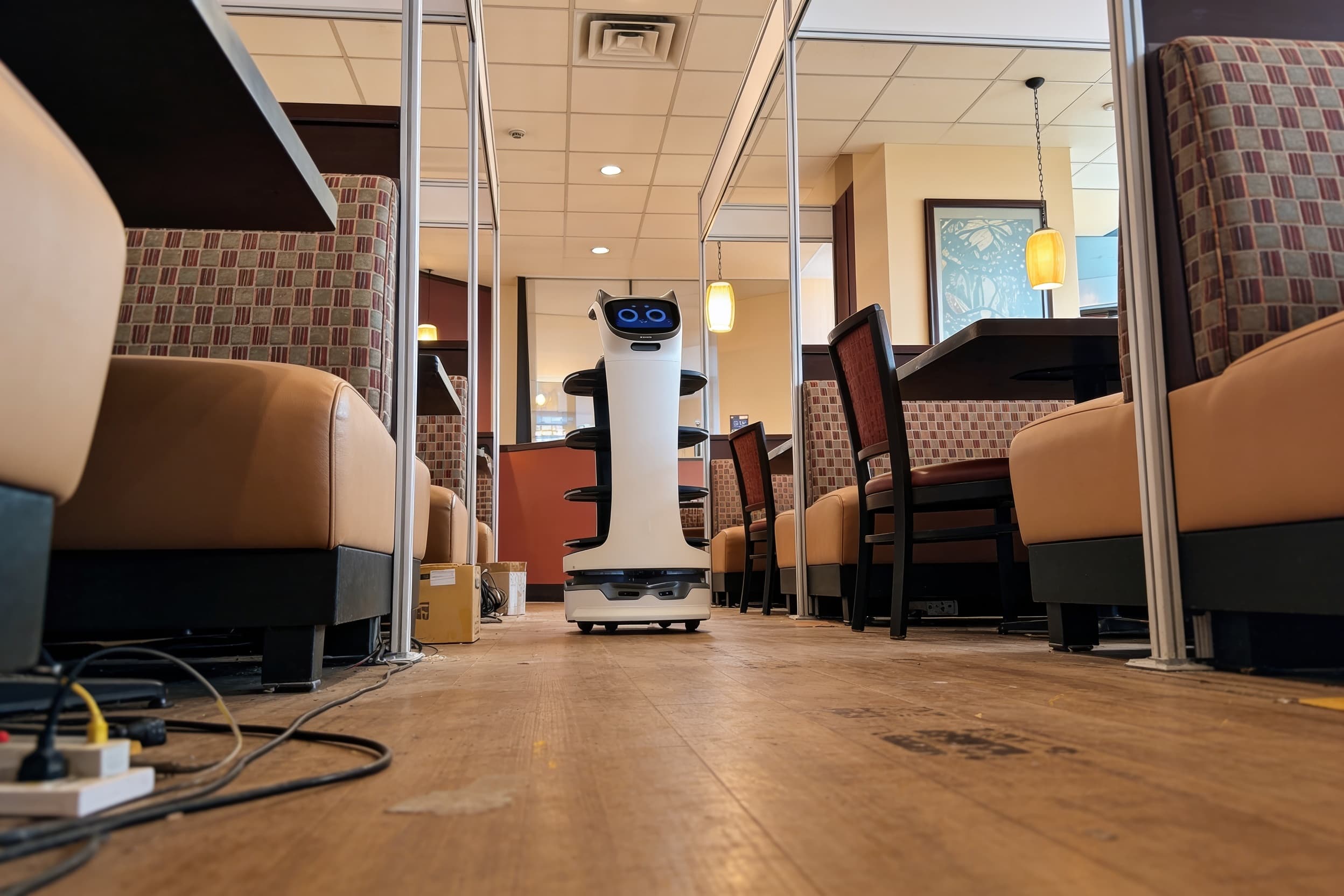 A serving robot running a plated dish between restaurant booths